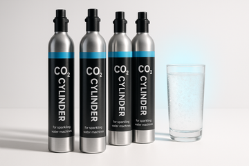 A modern product photo of CO₂ cylinders for sparkling water machines, styled in SodaStream colors (sleek silver metal with black and light blue details). Cylinders standing upright on a minimal white background with soft shadows. A clear glass of sparkling water with fizzy bubbles and a light blue accent glow in the background, suggesting freshness. Bright, high-resolution ecommerce photography, clean and professional style, with a premium look.